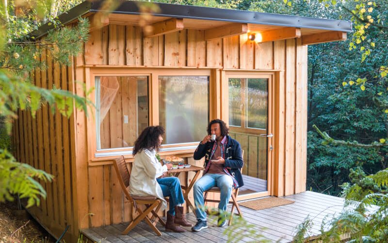 Full length shot of Hispanic couple having coffee on a patio of their glamping cabin.